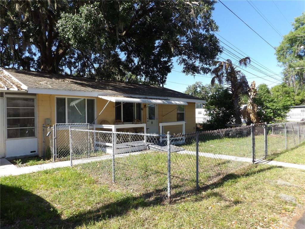 A yellow single-story house features a chain-link fence, a small porch, and large trees — 507 LAKE STREET, INVERNESS, FL