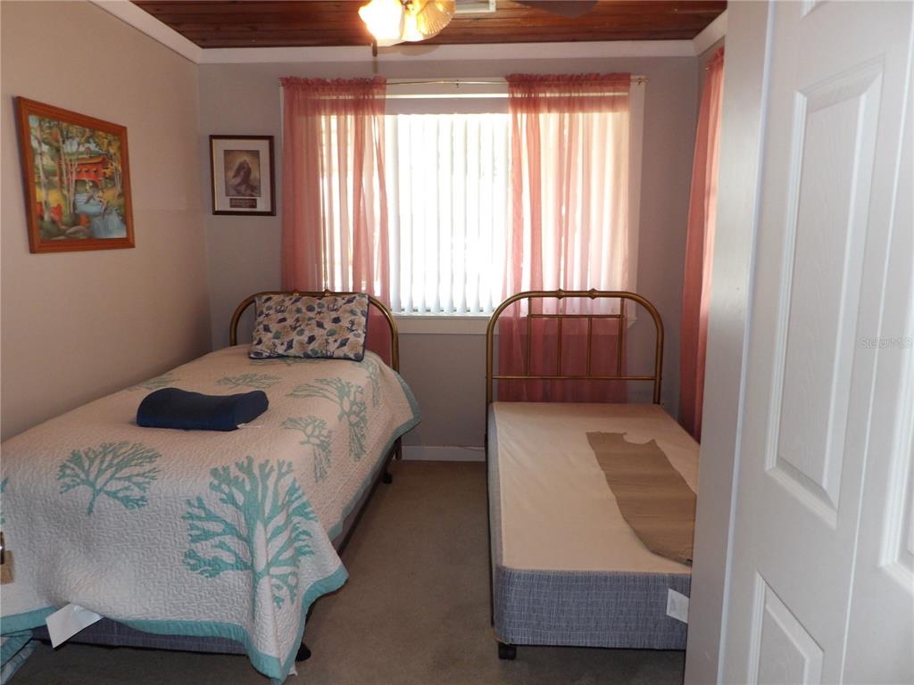 A bedroom features two twin beds, a window with pink curtains, and wood-paneled ceilings — 507 LAKE STREET, INVERNESS, FL