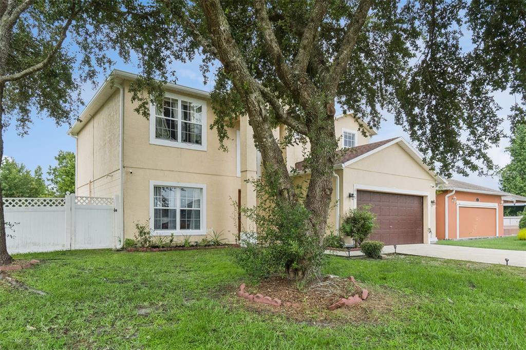 A two-story tan stucco house with a brown garage and a large tree in front — 610 NOTRE DAME WAY, KISSIMMEE, FL