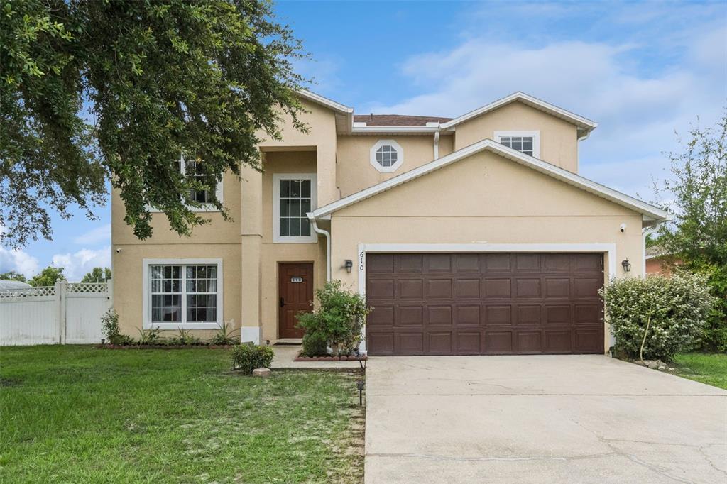 A two-story stucco house features a brown garage door, a front entrance, and a lawn — 610 NOTRE DAME WAY, KISSIMMEE, FL