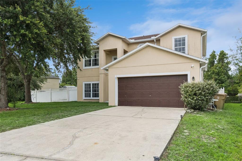 A two-story tan stucco house features a brown two-car garage and a concrete driveway — 610 NOTRE DAME WAY, KISSIMMEE, FL