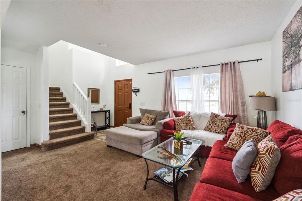 A living room features brown carpeting, a red sectional sofa, a staircase, and a front door — 610 NOTRE DAME WAY, KISSIMMEE, FL