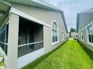 A side view of a house exterior featuring a screened-in porch and a grassy yard — 2206 CYPRESS KNEE LOOP, KISSIMMEE, FL