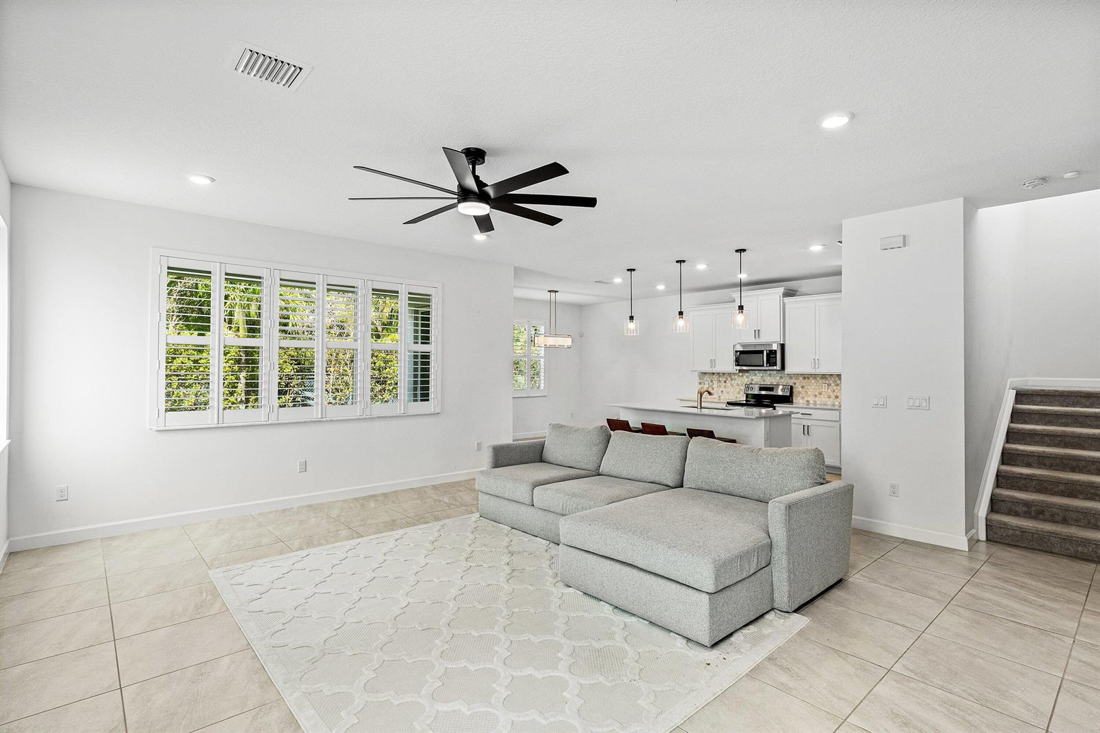 A bright open-concept living room features a grey sectional sofa, tile flooring, and a kitchen — 2659 Country Lake Trail, Boynton Beach FL 33436, BOYNTON BEACH, FL
