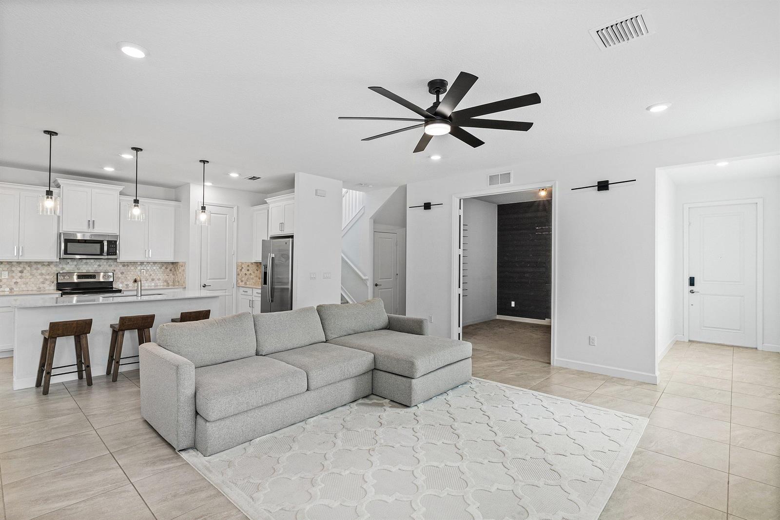 A modern open-concept living room and kitchen featuring a grey sectional, white cabinets, and tile — 2659 Country Lake Trail, Boynton Beach FL 33436, BOYNTON BEACH, FL