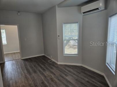 An interior room with light gray walls, wood-look flooring, two windows, and a wall-mounted air conditioner — 306 TURNER STREET UNIT 1, CLEARWATER, FL