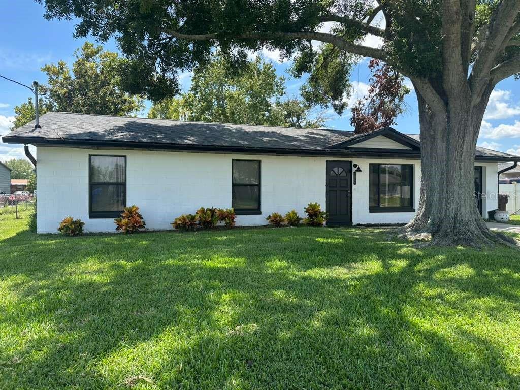 A single-story white concrete block house with a dark roof and black window trim — 1524 MANOR DRIVE, KISSIMMEE, FL