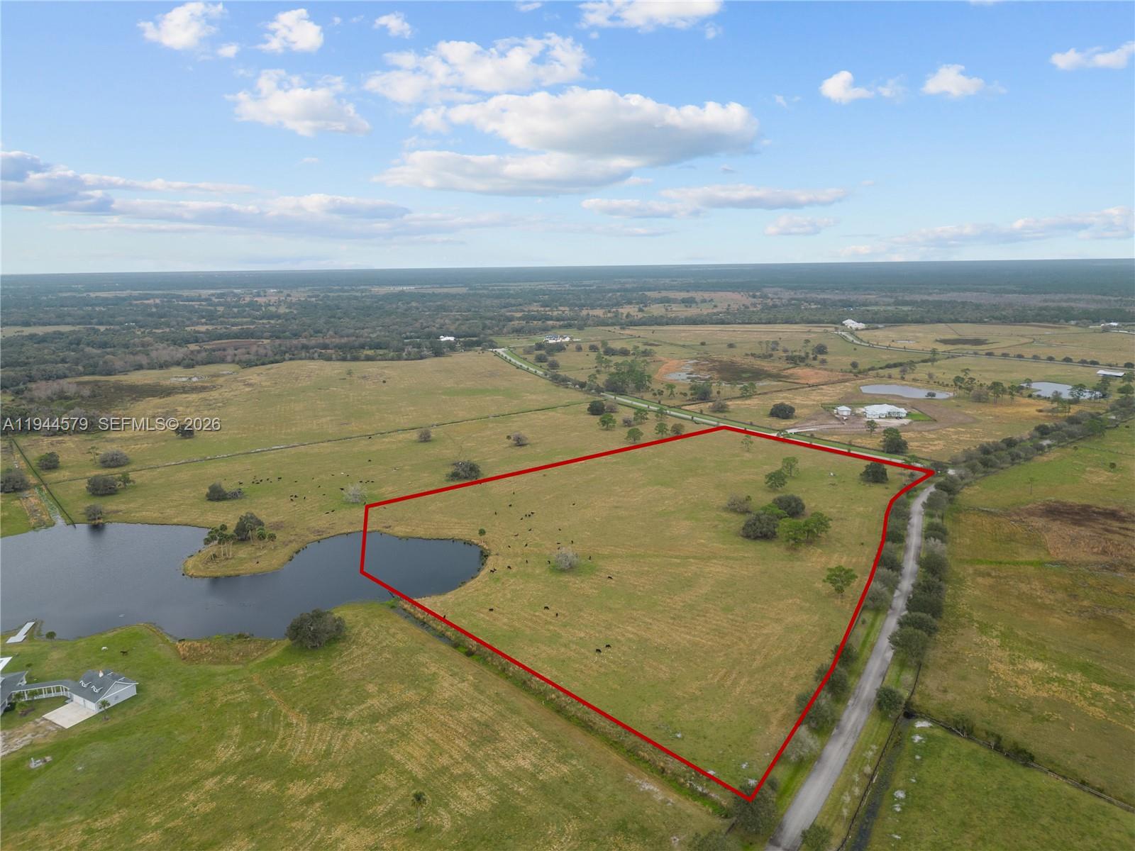 An aerial view shows a large, fenced-in grassy pasture with a pond and road access — 25750 SW Jockeys Run, Okeechobee FL 34974, OKEECHOBEE, FL