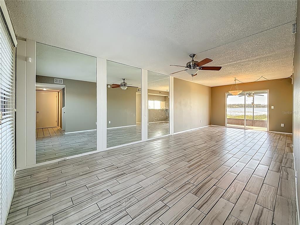 A living room features wood-look tile flooring, a mirrored wall, and a sliding glass door — 9209 SEMINOLE BOULEVARD UNIT 32, SEMINOLE, FL