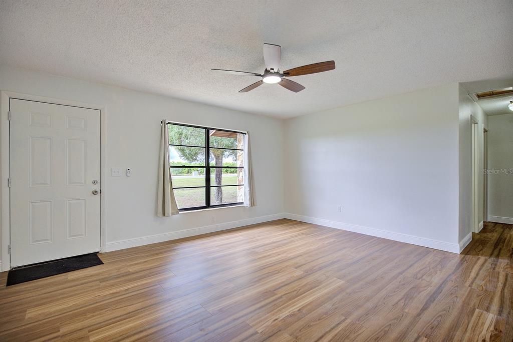 An empty room features light-colored walls, wood-look flooring, a ceiling fan, and a front door — 2052 W STRYKER ROAD, AVON PARK, FL