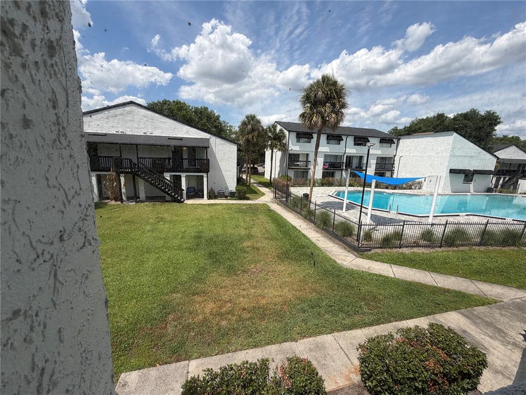 An exterior view of apartment buildings with a grassy courtyard and a fenced swimming pool — 4215 S SEMORAN BOULEVARD UNIT 15, ORLANDO, FL