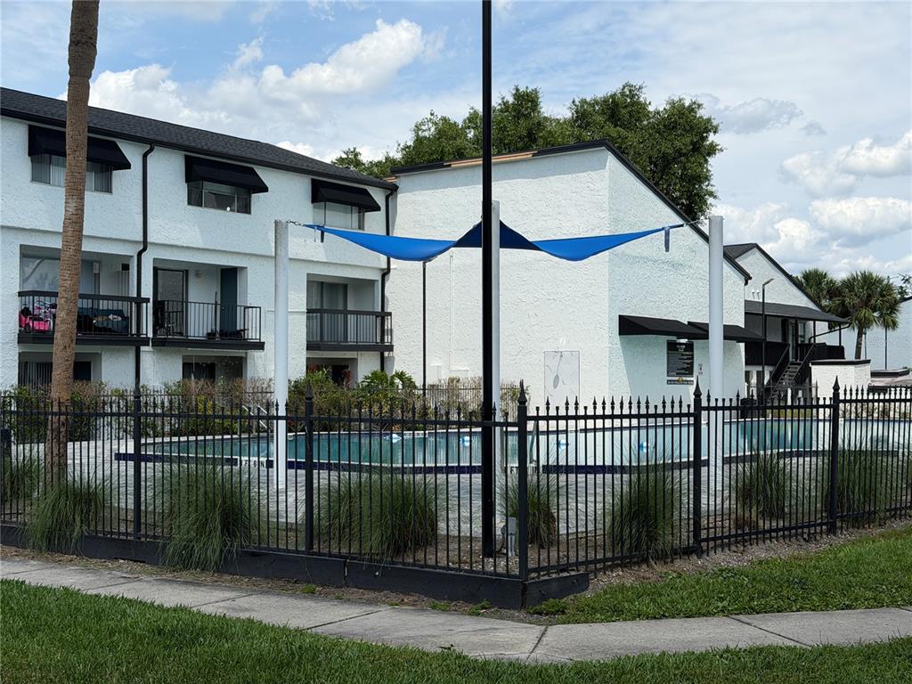 A swimming pool with a blue shade sail is enclosed by a black metal fence — 4215 S SEMORAN BOULEVARD UNIT 15, ORLANDO, FL