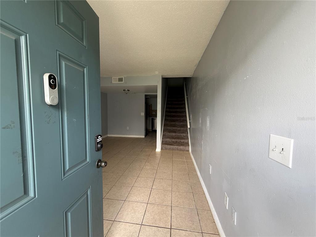 An open doorway reveals a tiled entryway leading to a carpeted staircase and living area — 4215 S SEMORAN BOULEVARD UNIT 15, ORLANDO, FL
