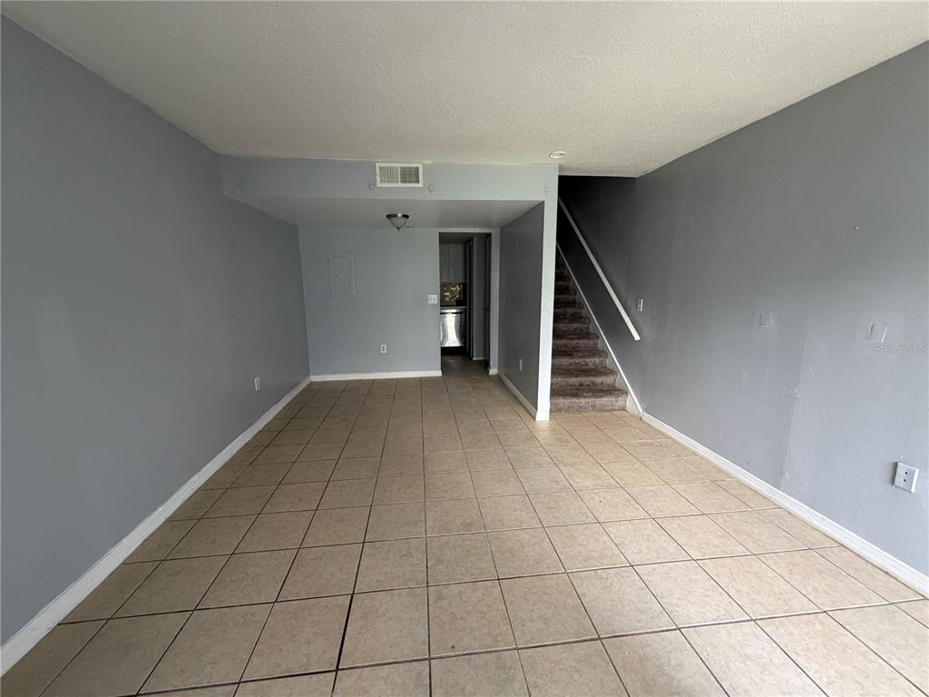 An empty room with light-colored tile flooring, gray walls, and a staircase leading upstairs — 4215 S SEMORAN BOULEVARD UNIT 15, ORLANDO, FL