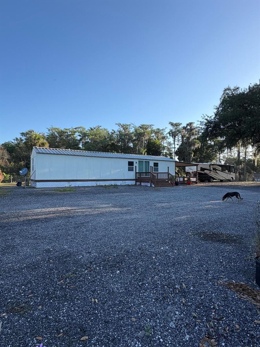 A mobile home with a wooden deck and an adjacent RV sit on a gravel lot — 855 N Datil Street, Clewiston FL 33440, CLEWISTON, FL
