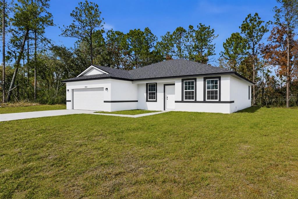 A single-story white house with a dark roof and a two-car garage sits on grass — 15936 SW 35TH COURT ROAD, OCALA, FL