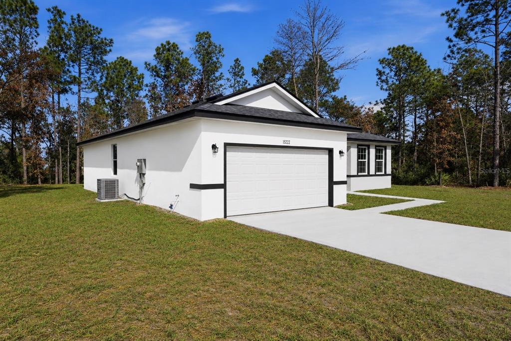 A white single-story house with a black roof and garage door sits on a grassy lot — 15936 SW 35TH COURT ROAD, OCALA, FL