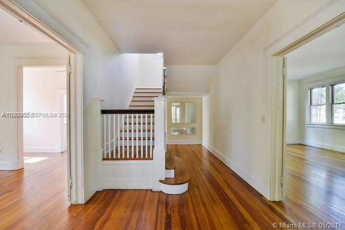 A staircase with a white railing and wooden steps sits between two rooms with hardwood floors — 2000 S Miami Ave, Miami FL 33129, MIAMI, FL