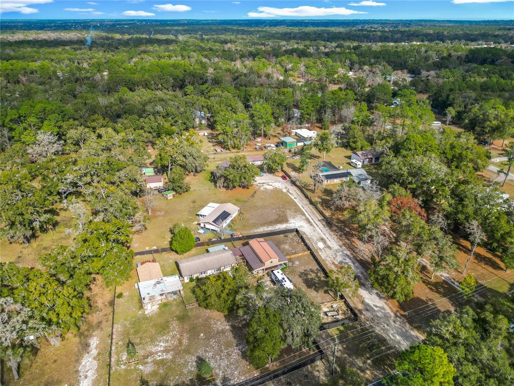 A white, single-story concrete block house features a brown shingled roof with solar panels — 11859 W HIGHWAY 328, OCALA, FL
