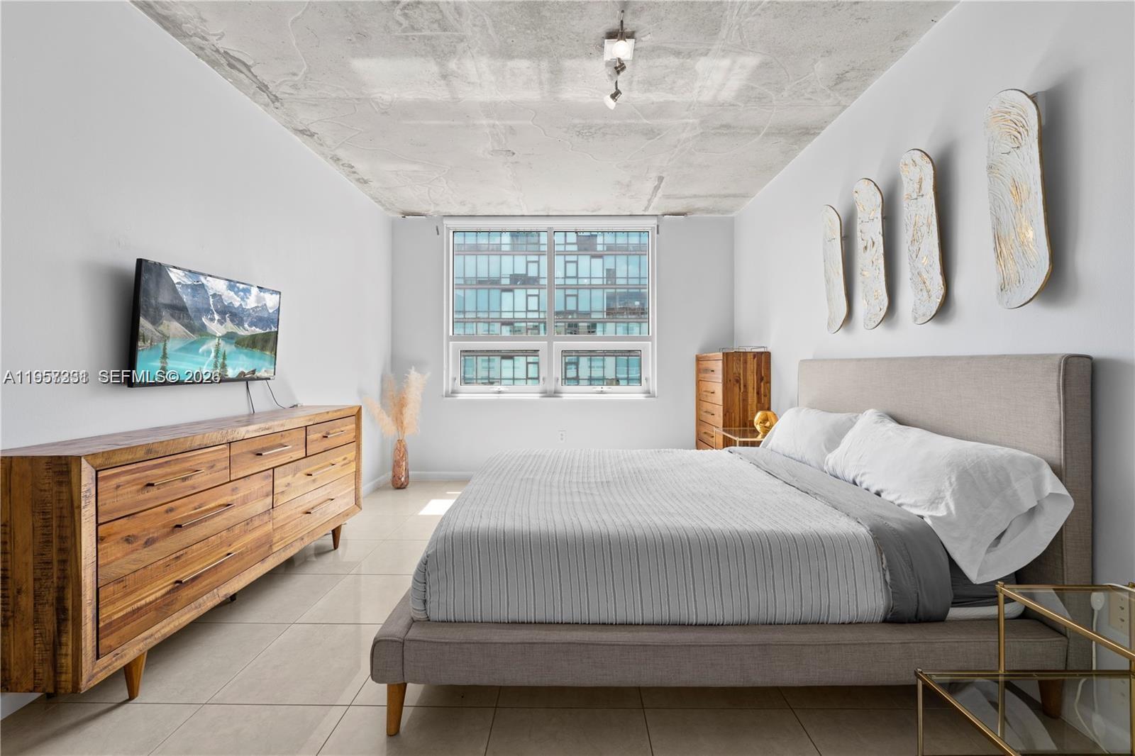 A bedroom features a concrete ceiling, tiled floors, a wooden dresser, and a gray bed — 3250 NE 1st Ave # 917, Miami FL 33137, MIAMI, FL