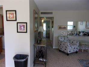 A living area features a patterned armchair, a console table, and a hallway leading inward — 1811 BEDFORD LANE UNIT 164, SUN CITY CENTER, FL