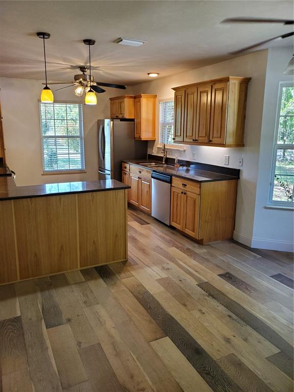 A kitchen features wood cabinets, dark countertops, stainless steel appliances, and multi-toned wood flooring — 22819 NW 209TH TERRACE, HIGH SPRINGS, FL