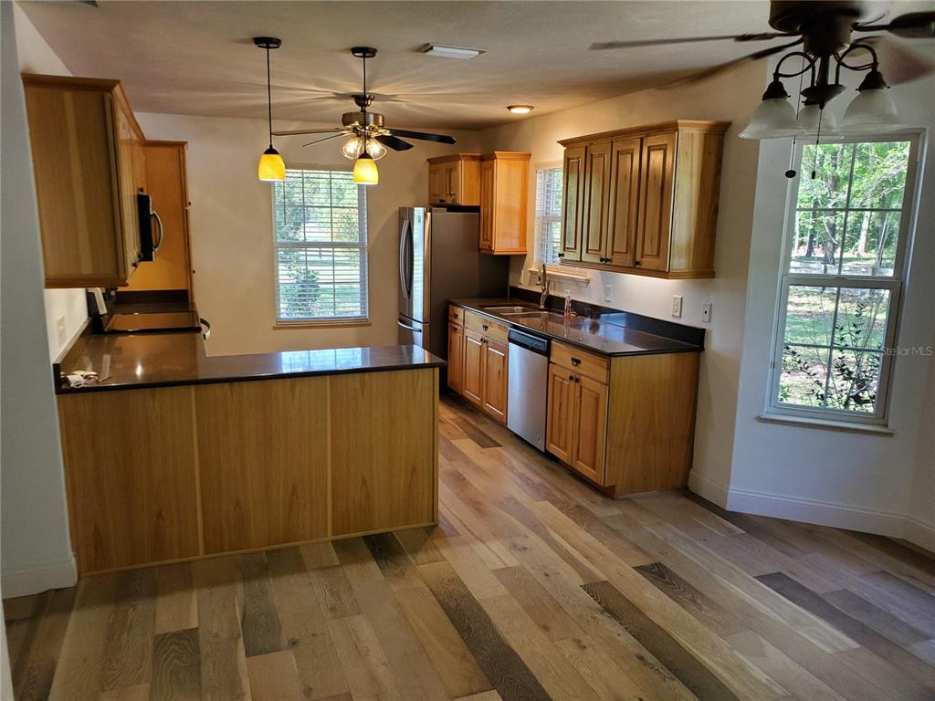 A kitchen features wood cabinets, dark countertops, stainless steel appliances, and light-toned wood flooring — 22819 NW 209TH TERRACE, HIGH SPRINGS, FL