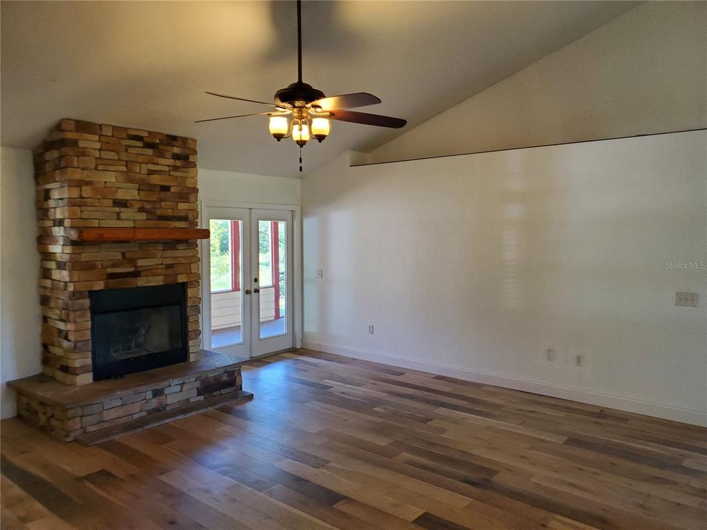 A living room features a stone fireplace, wood flooring, a ceiling fan, and glass doors — 22819 NW 209TH TERRACE, HIGH SPRINGS, FL