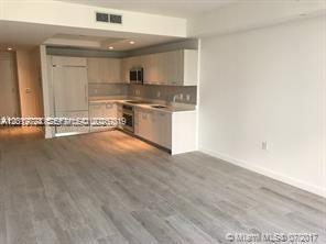 A modern kitchen with light wood cabinets and stainless steel appliances opens to a living area — 55 SW 9th St # 2504, Miami FL 33130, MIAMI, FL
