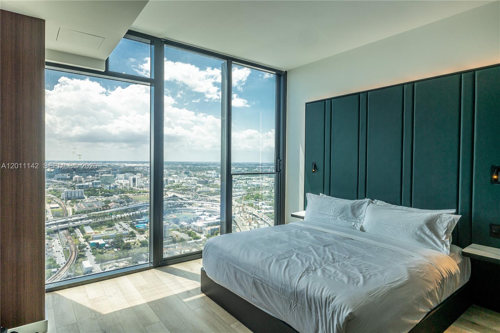 A bedroom features a large bed against a dark green headboard and floor-to-ceiling windows — 20 NE 11th st # 5306, Miami FL 33132, MIAMI, FL