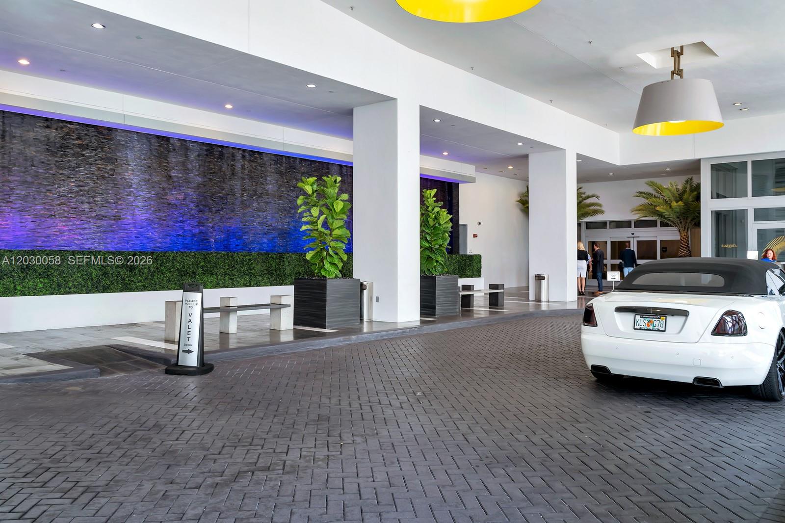 A white car is parked under a modern building entrance with a stone water feature — 1100 Biscayne Blvd # 5203, Miami FL 33132, MIAMI, FL