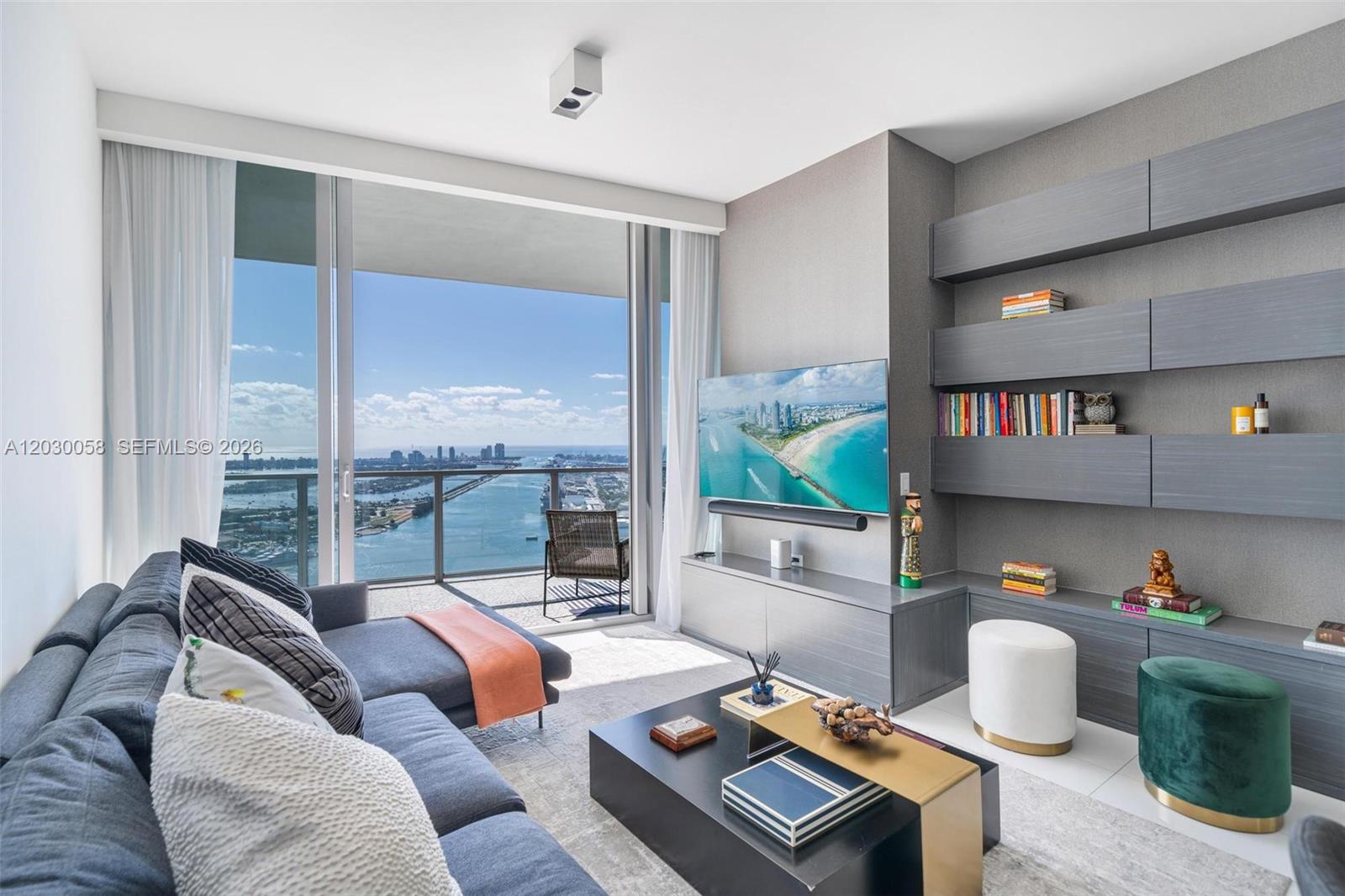A modern living room features a sectional sofa, built-in shelving, and a balcony with water views — 1100 Biscayne Blvd # 5203, Miami FL 33132, MIAMI, FL