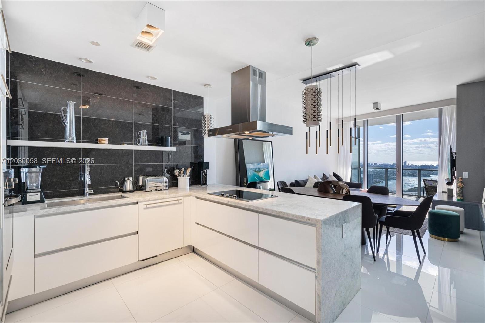 A modern kitchen features white cabinetry, a marble-topped island, and a dark tiled backsplash — 1100 Biscayne Blvd # 5203, Miami FL 33132, MIAMI, FL