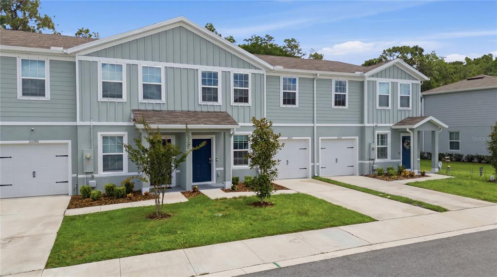 A row of two-story townhomes with light blue siding, white trim, and attached single-car garages — 12034 GRIZZLY LANE, NEW PORT RICHEY, FL