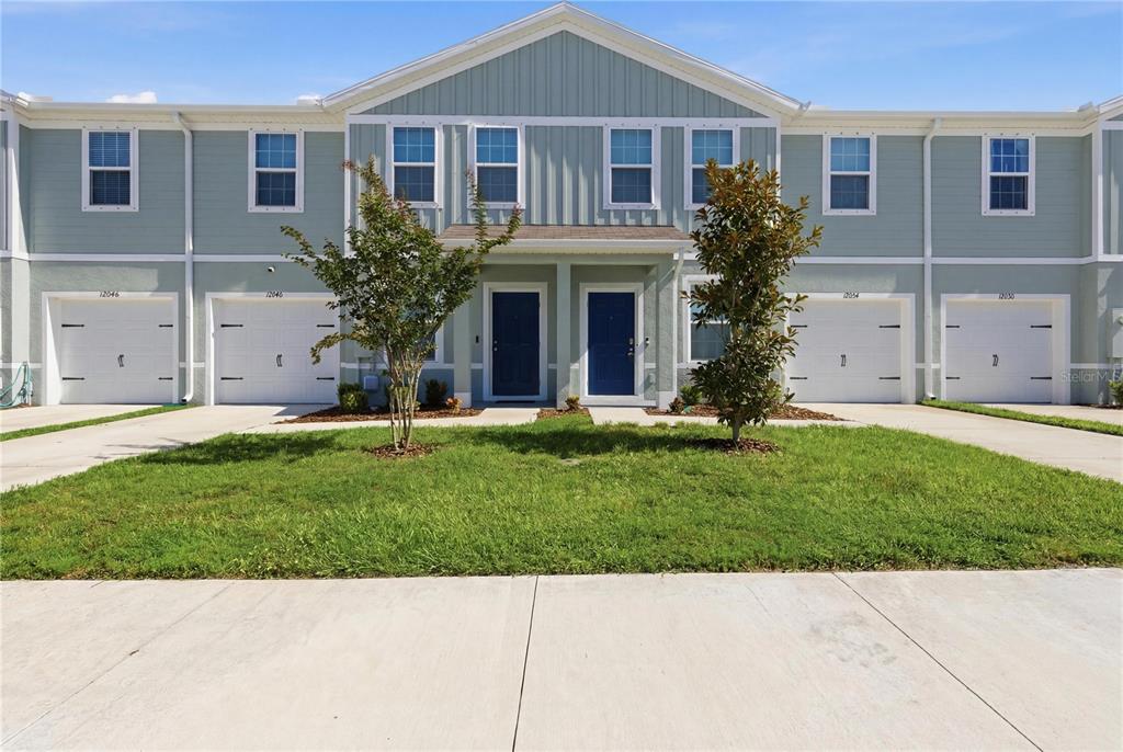 A two-story townhouse exterior with light green siding, white trim, and four garage doors — 12034 GRIZZLY LANE, NEW PORT RICHEY, FL