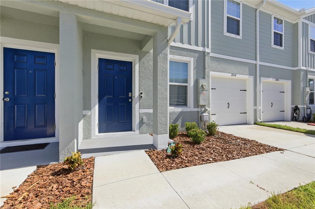 The exterior of a townhouse features blue front doors, white garage doors, and landscaped mulch — 12034 GRIZZLY LANE, NEW PORT RICHEY, FL