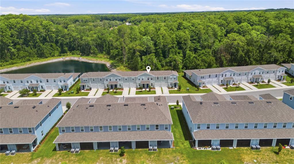 An aerial view shows several rows of light blue townhomes with brown roofs near a pond — 12034 GRIZZLY LANE, NEW PORT RICHEY, FL