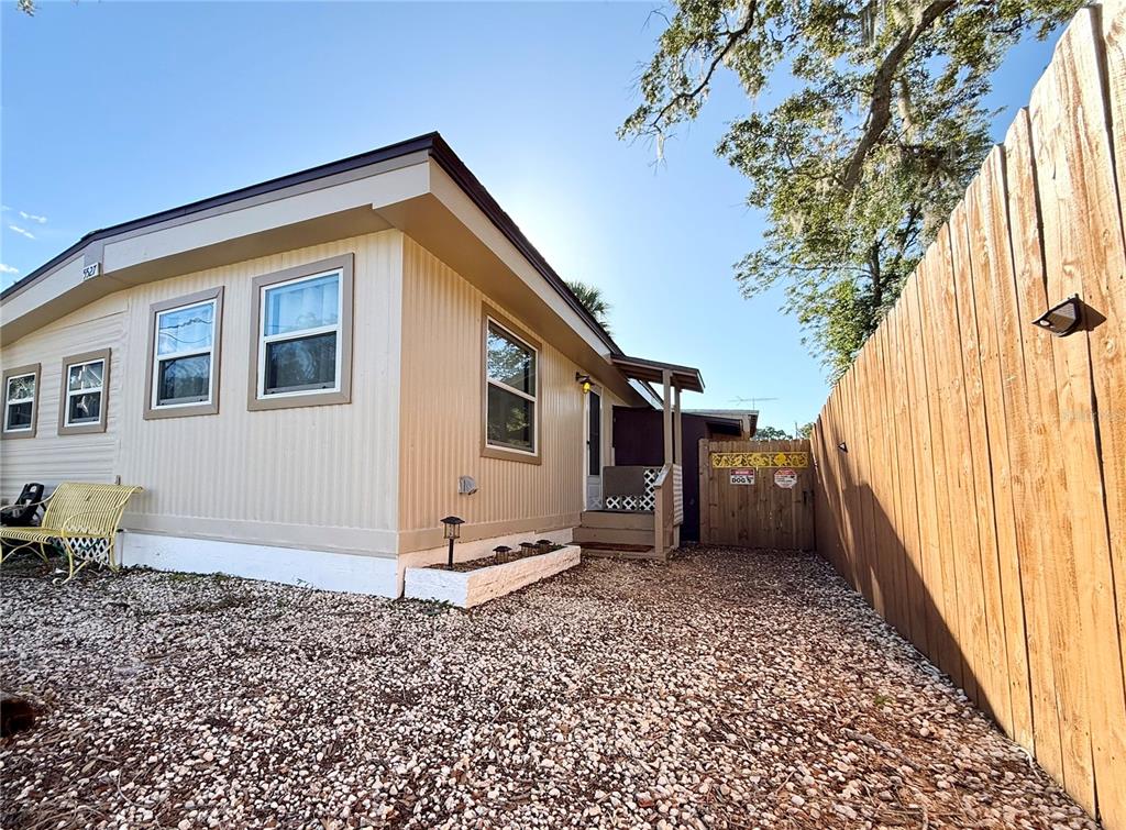 The exterior of a tan mobile home features a gravel yard and a wooden fence — 5527 DARLENE STREET, WEEKI WACHEE, FL
