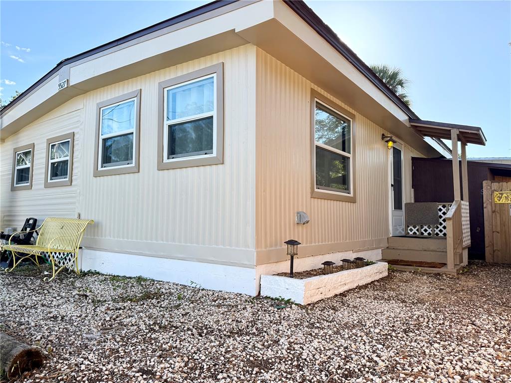 The exterior of a beige mobile home features a gravel yard and a small porch — 5527 DARLENE STREET, WEEKI WACHEE, FL
