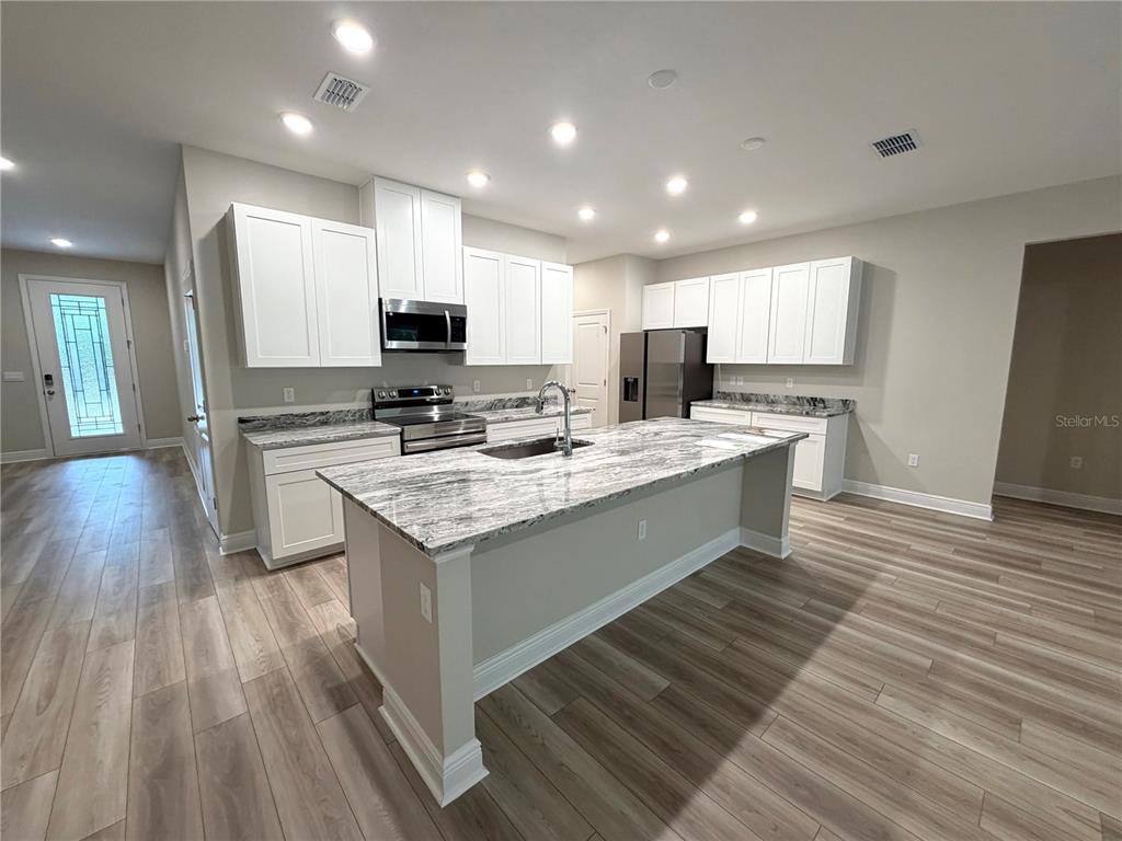 A modern kitchen features white cabinets, a large granite island, and light wood-look flooring — 11059 N MORRELL DRIVE, CITRUS SPRINGS, FL