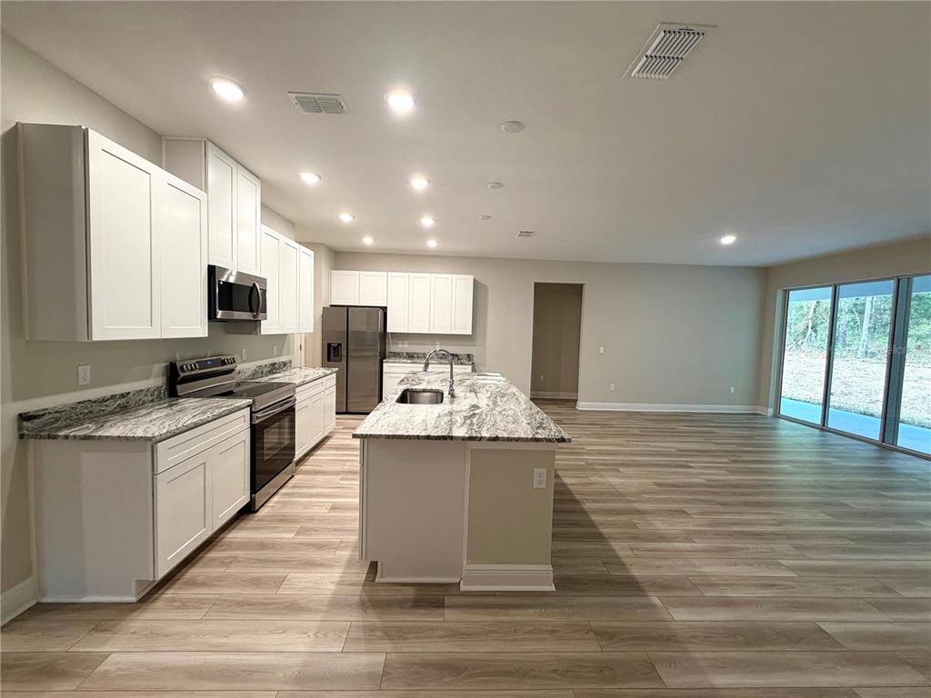 A modern kitchen features white cabinets, granite countertops, a central island, and wood-look flooring — 11059 N MORRELL DRIVE, CITRUS SPRINGS, FL
