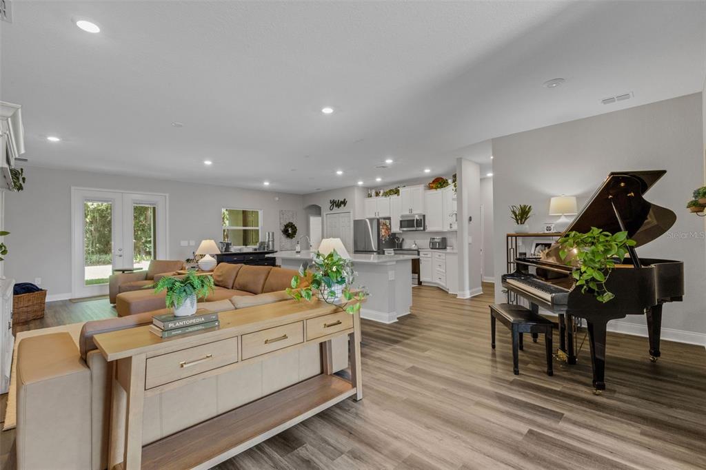 An open-concept living room and kitchen featuring a grand piano, sectional sofa, and wood flooring — 2980 KEENS GROVE WAY, LAKELAND, FL