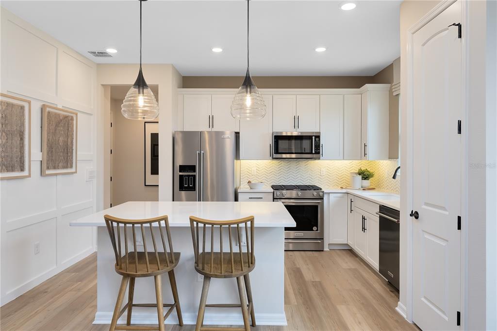 A modern kitchen features white cabinetry, a central island with two chairs, and stainless appliances — 2841 MIDSWEET AVENUE, ST CLOUD, FL