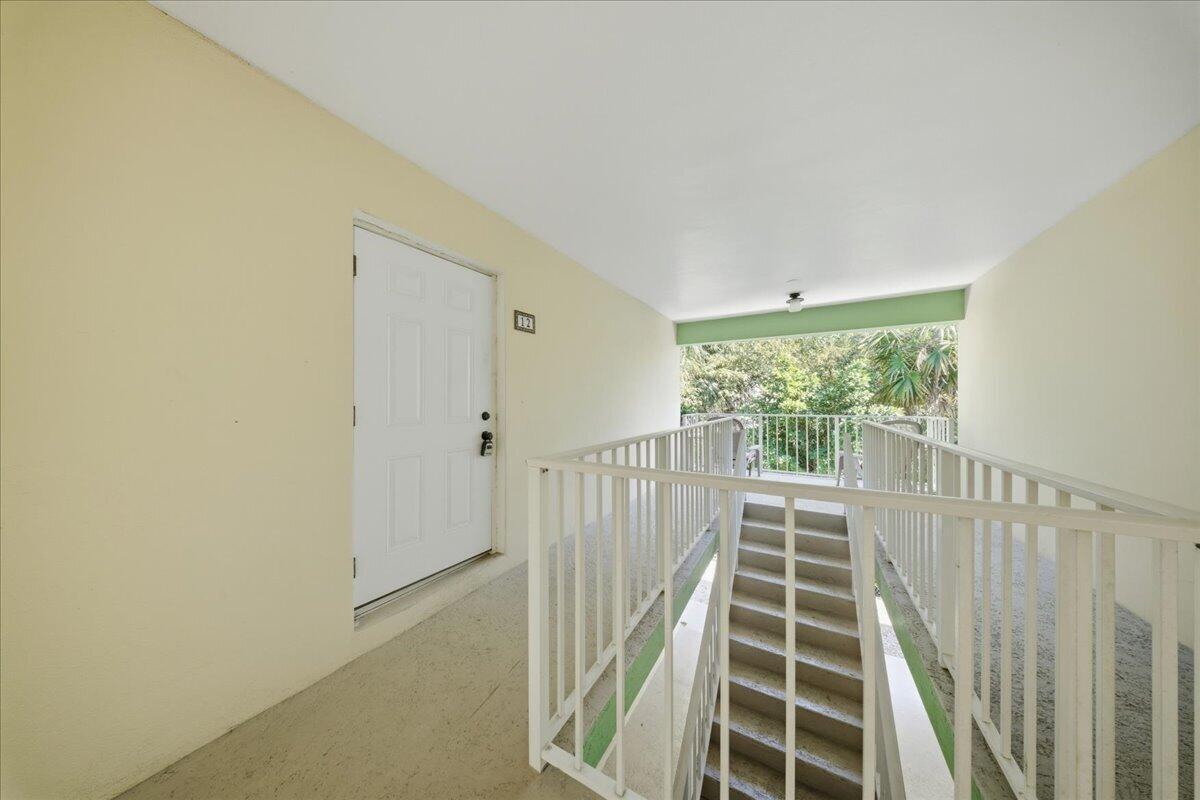 An outdoor apartment hallway features a white door, a staircase, and a metal railing — 1129 Pebble Beach Lane # 12, FL 33050, FL