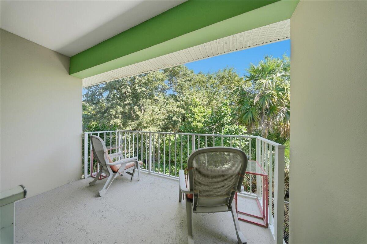 A covered balcony features a white metal railing, two rocking chairs, and a view of trees — 1129 Pebble Beach Lane # 12, FL 33050, FL