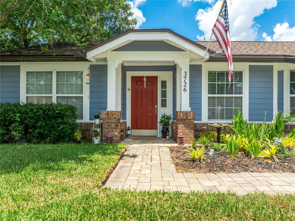 A blue house with a red front door, brick accents, and an American flag — 3726 SARASOTA COURT, ORLANDO, FL