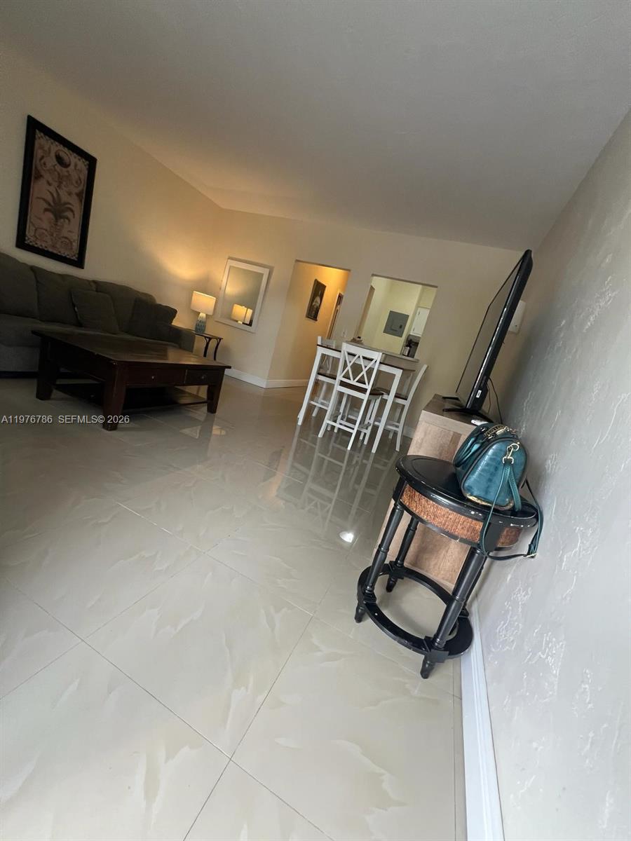 This living and dining area features tile flooring, a gray sofa, and a wooden table — 600 Layne Blvd # 210, Hallandale Beach FL 33009, HALLANDALE BEACH, FL