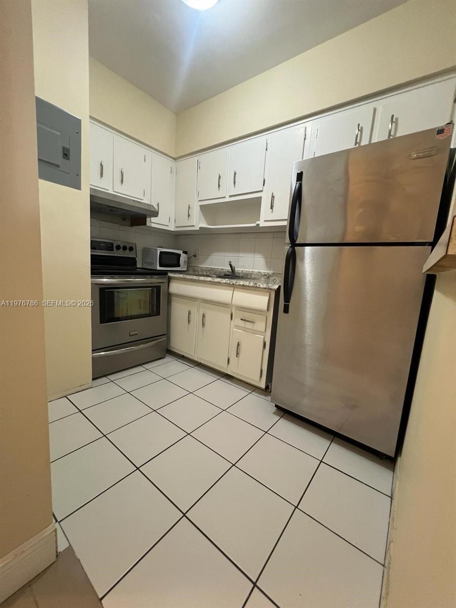 A kitchen features white cabinets, stainless steel appliances, and light-colored floor tiles — 600 Layne Blvd # 210, Hallandale Beach FL 33009, HALLANDALE BEACH, FL