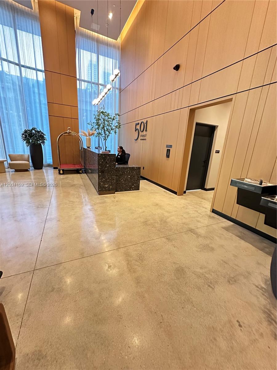 A modern building lobby features a reception desk, tall windows, and wood-paneled walls — 121 NE 5 # 2712, Miami FL 33132, MIAMI, FL