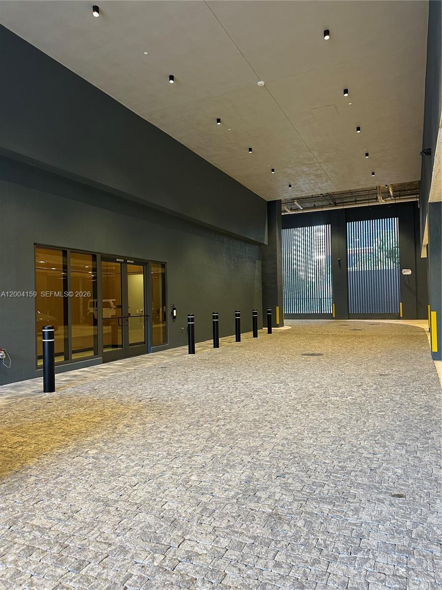 A paved driveway leads to a modern building entrance with glass doors and recessed lighting — 121 NE 5 # 2712, Miami FL 33132, MIAMI, FL